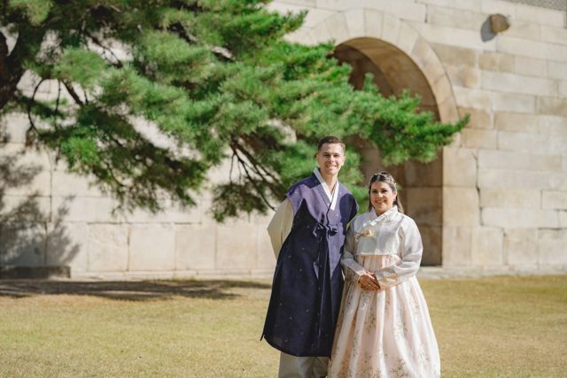 Couple in hanbok by a stone palace wall under a pine tree