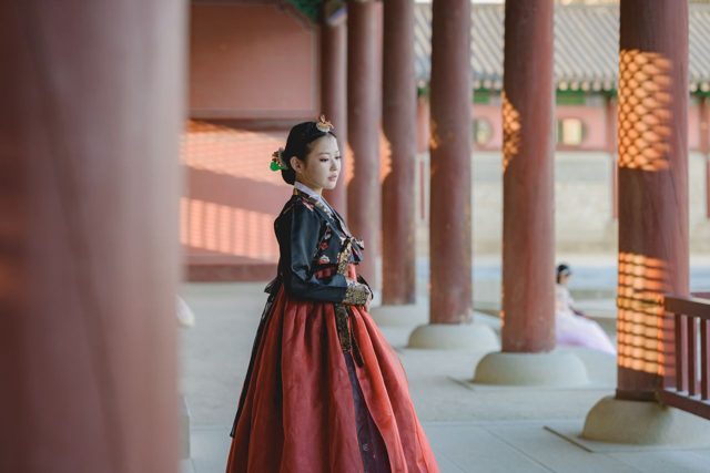 Woman in a red and black hanbok among palace pillars