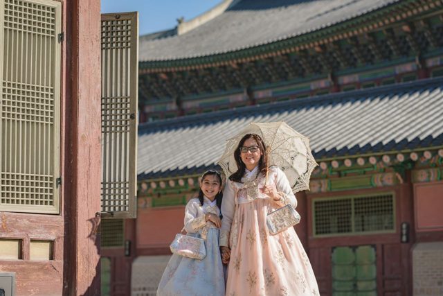 Two family members in hanbok with a lace parasol at a palace